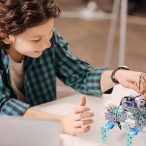 Robot of the future. Capable delighted positive boy sitting at school and using digital gadget while studying and expressing joy