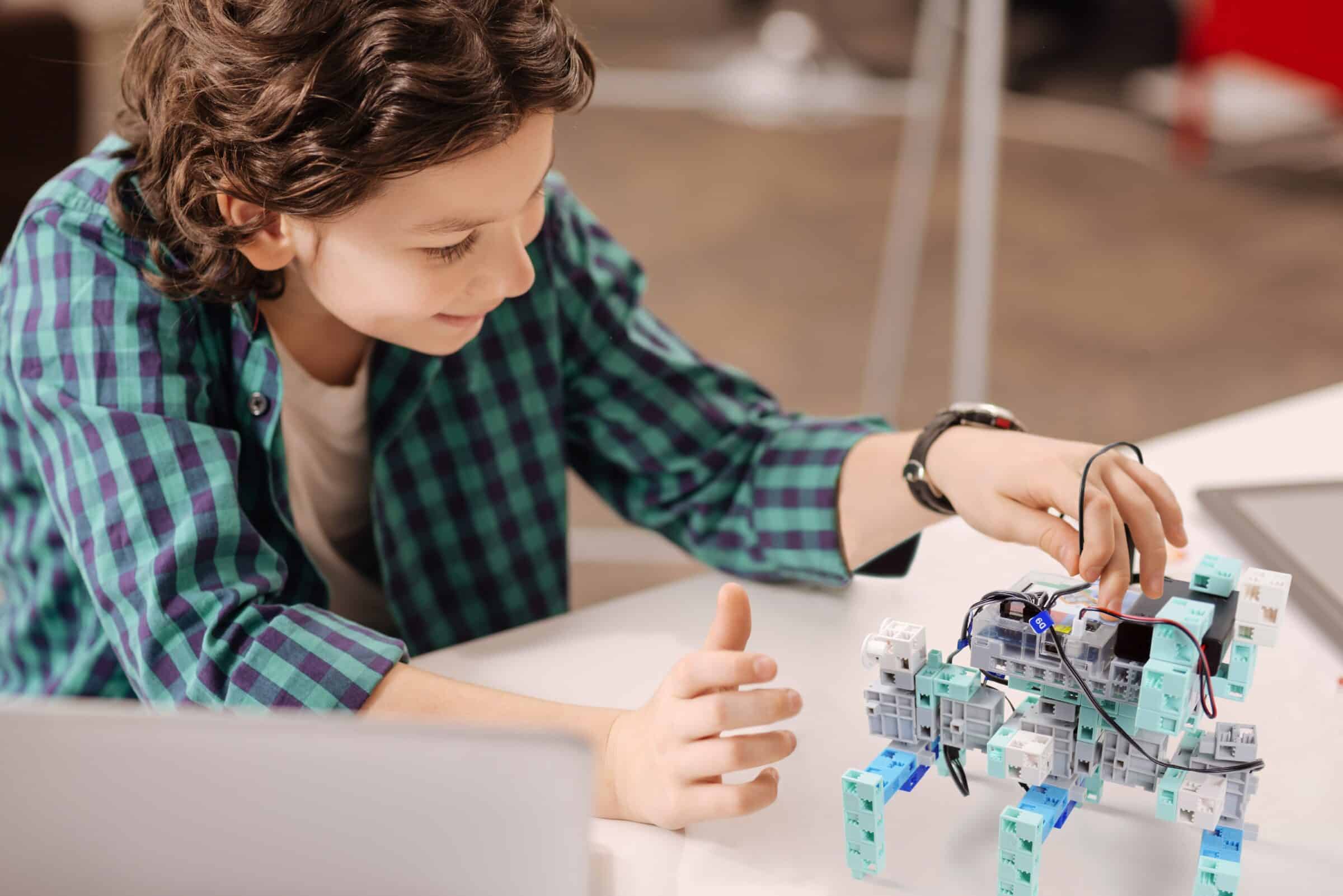 Robot of the future. Capable delighted positive boy sitting at school and using digital gadget while studying and expressing joy