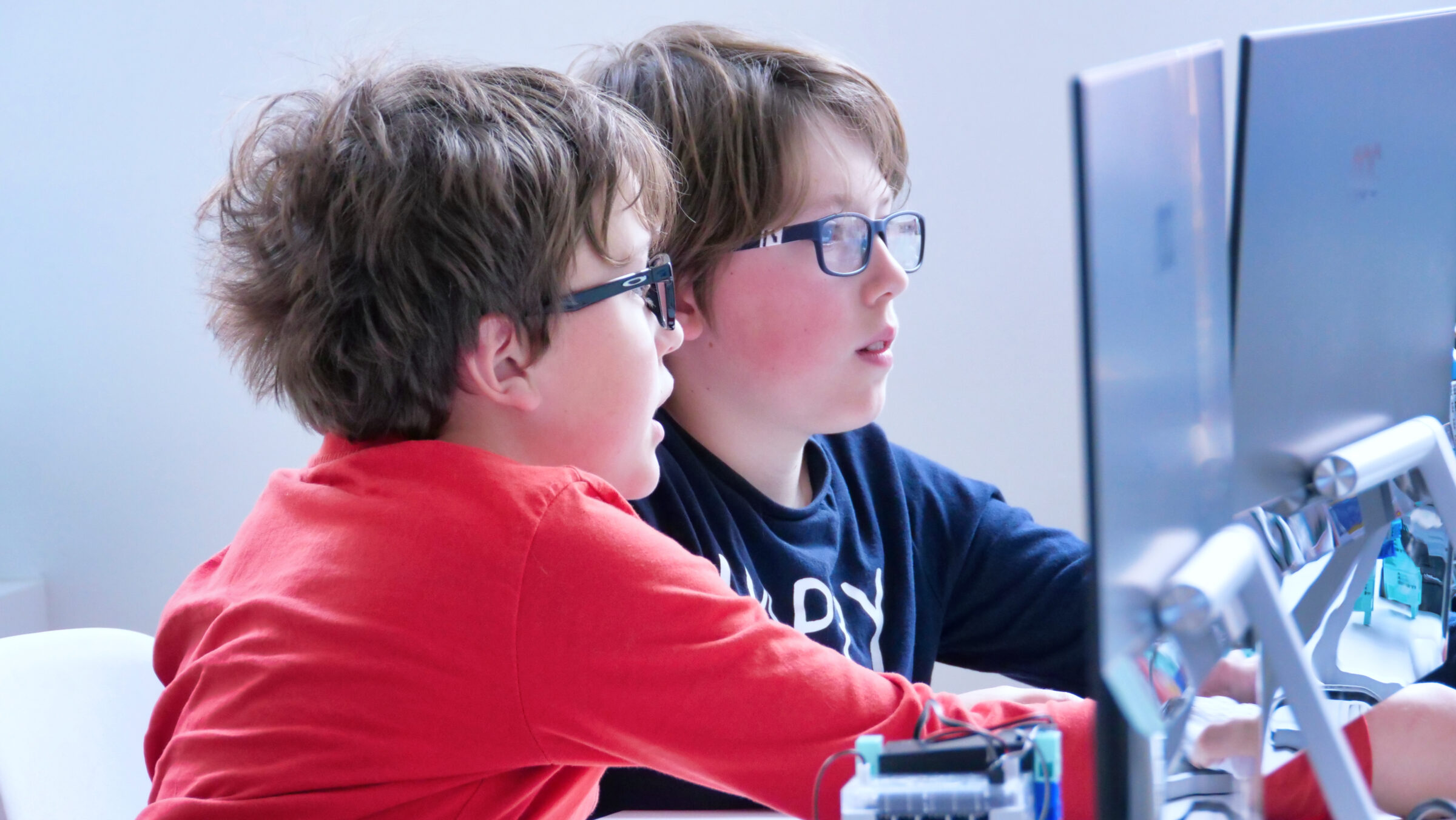 2 garçons à lunettes élaborant un code pour leur robot tyrannosaure lors d'un atelier robotic park